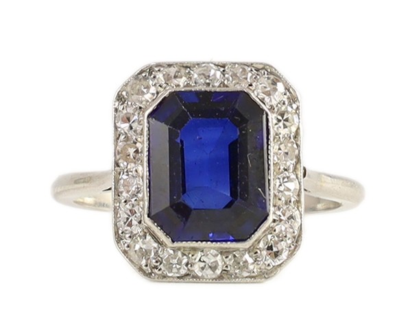 A 1920's platinum, emerald cut sapphire and millegrain set diamond rectangular cluster ring, with canted corners